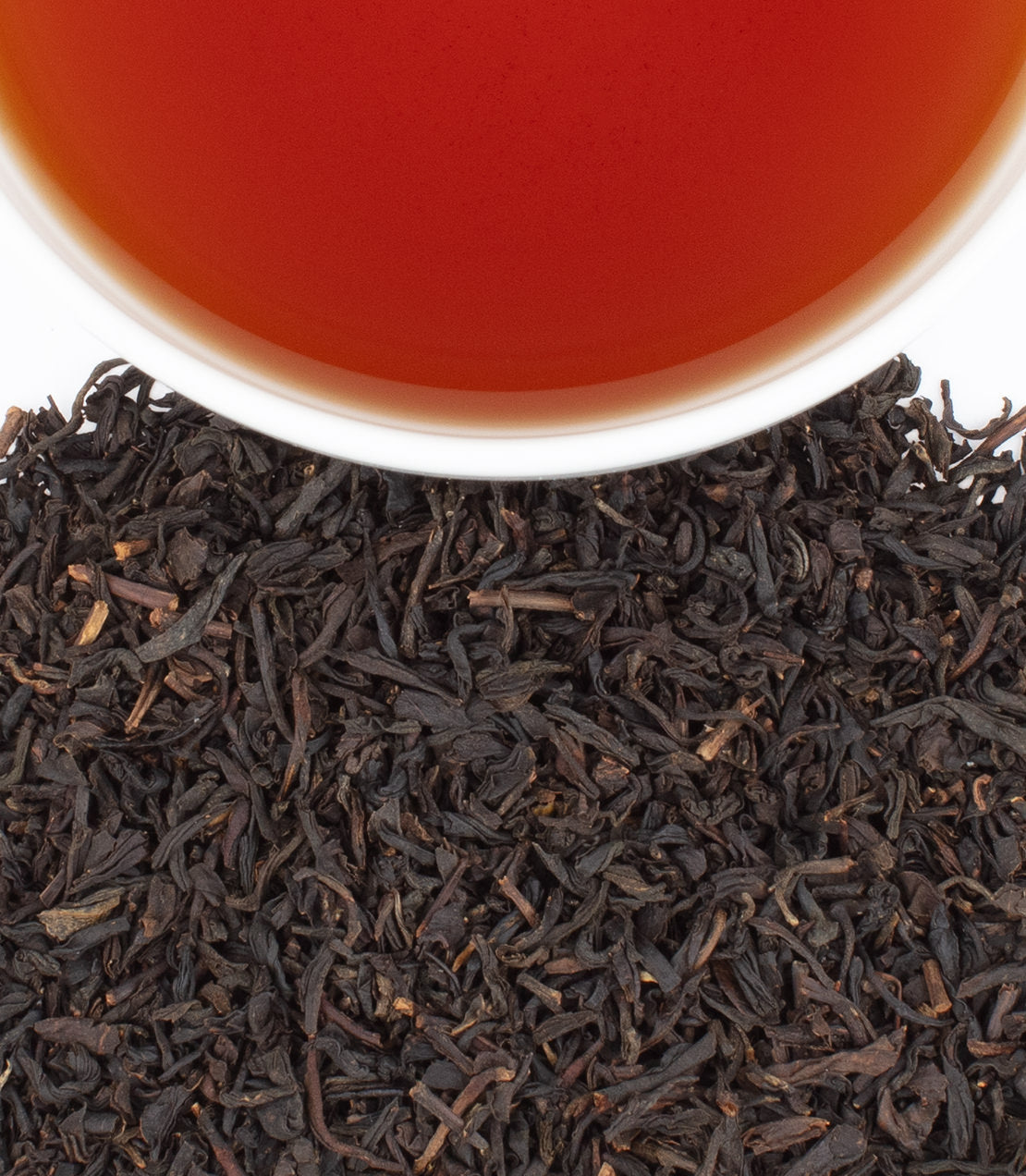Salted Caramel tea in a white cup, surrounded by loose black tea leaves, showcasing a rich amber color.