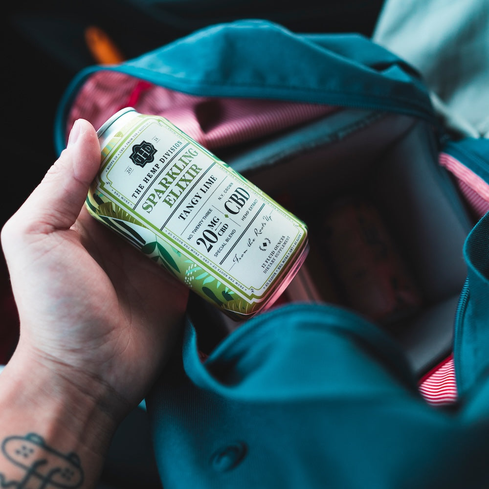 Hand holding a can of Sparkling Elixir with 20 MG Hemp, placed inside a bag, showcasing its vibrant design.
