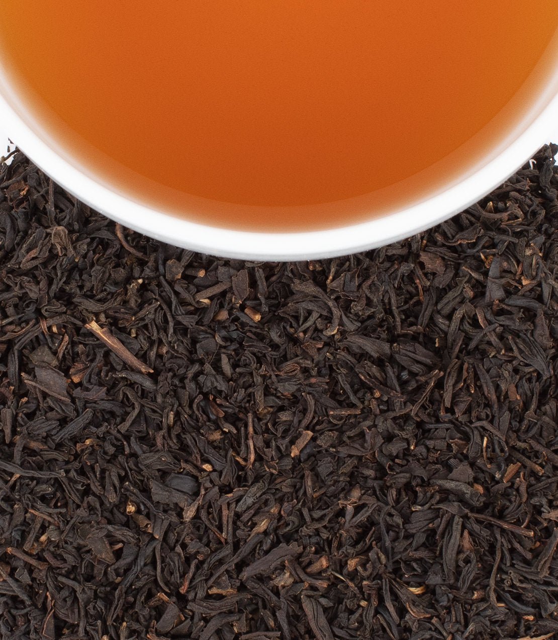 Black Cask Bourbon tea in a white cup, surrounded by loose black tea leaves, showcasing rich amber color.