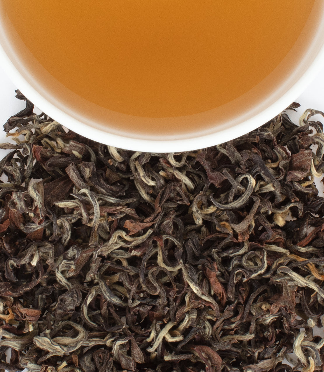 Nepalese hand-rolled tea tips with a cup of brewed tea, showcasing rich colors and textures.
