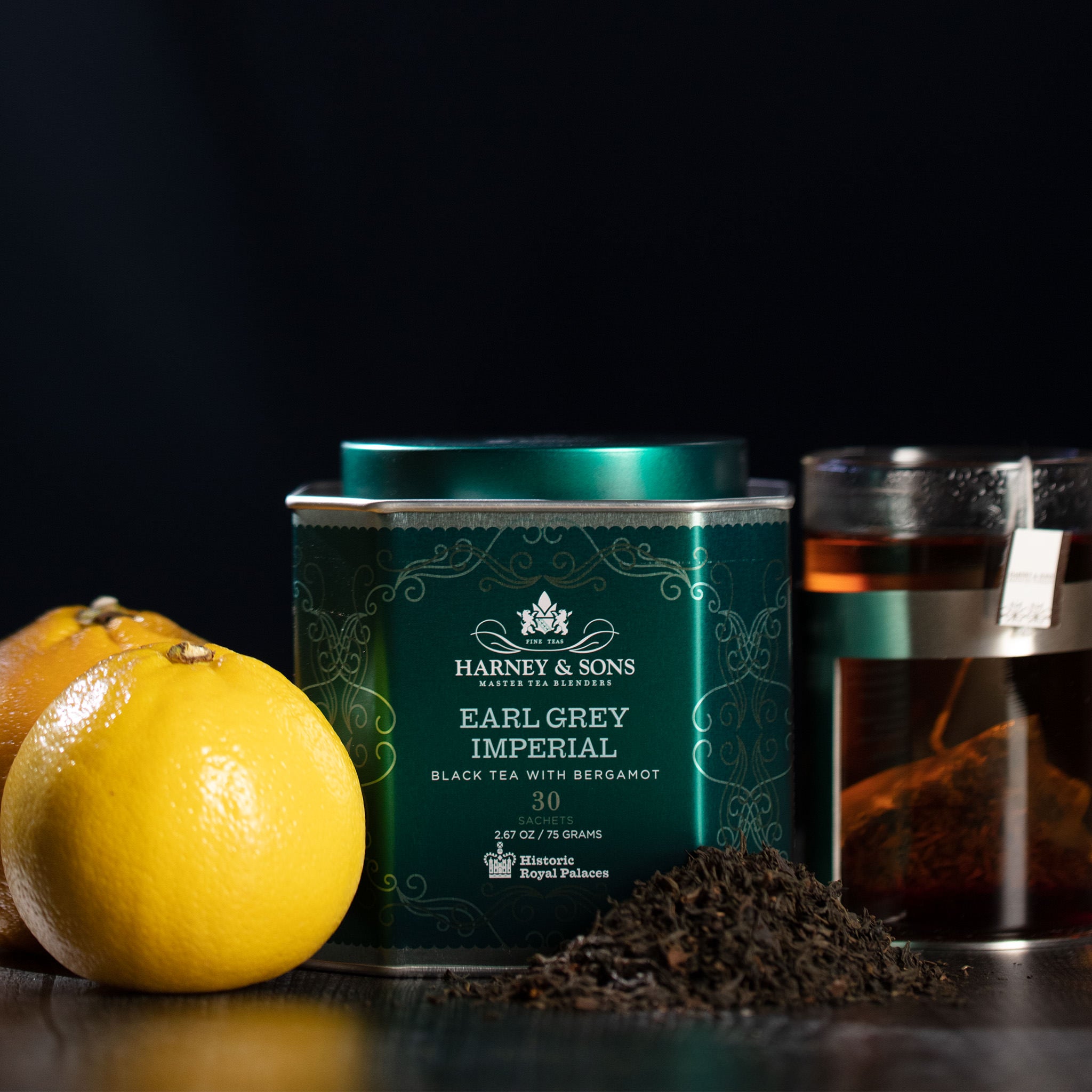 Harney & Sons Earl Grey Imperial tea tin with loose black tea, bergamot, and fresh oranges on a dark background.